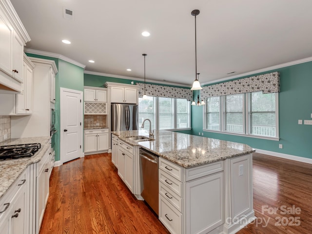 kitchen featuring decorative light fixtures, white cabinetry, a center island with sink, stainless steel appliances, and a sink