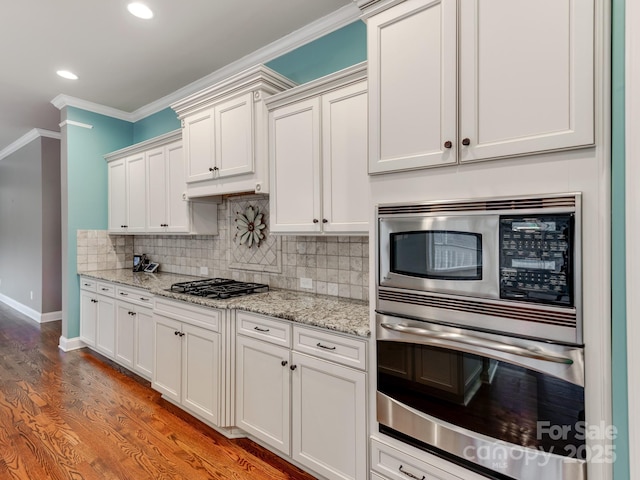 kitchen featuring white cabinets, light stone counters, appliances with stainless steel finishes, tasteful backsplash, and crown molding