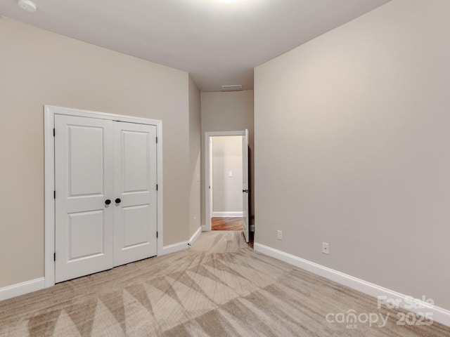 unfurnished bedroom with a closet, visible vents, light colored carpet, and baseboards