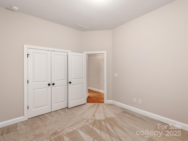 unfurnished bedroom featuring a closet, light colored carpet, and baseboards