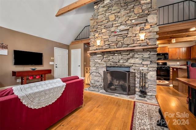 living room featuring beamed ceiling, a stone fireplace, light wood-type flooring, and high vaulted ceiling