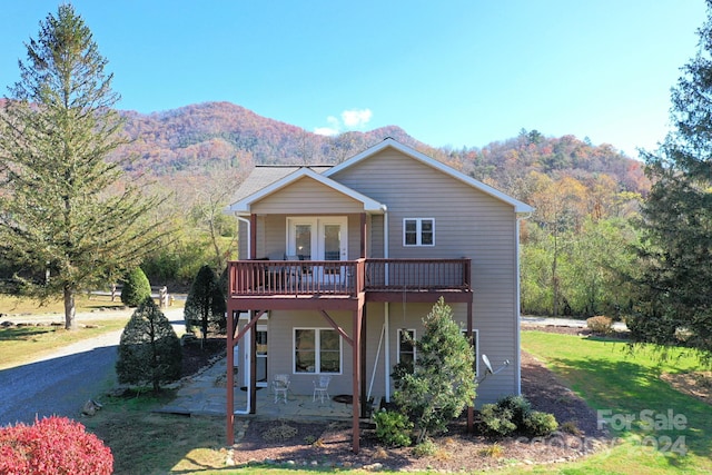 view of front property with a deck with mountain view, a patio, and a front yard