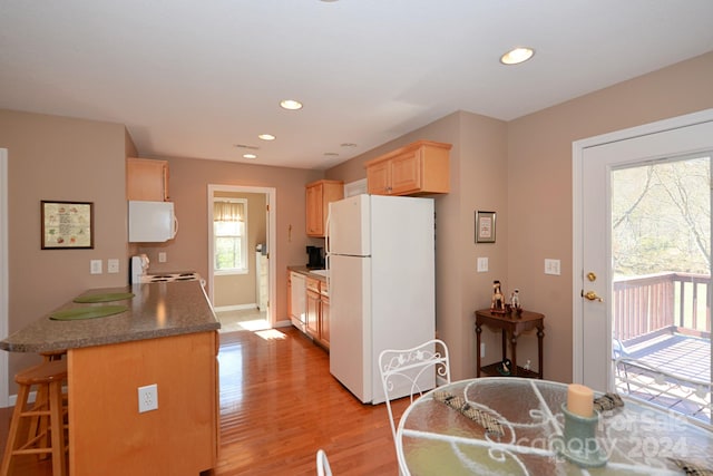 kitchen featuring light brown cabinetry, plenty of natural light, light hardwood / wood-style floors, and white appliances