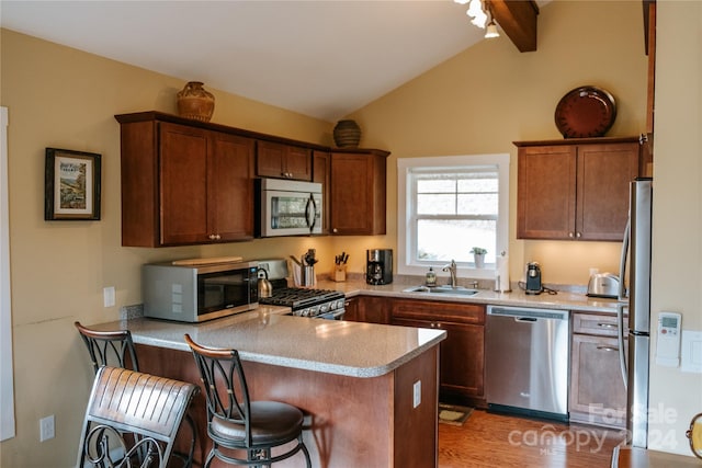 kitchen with sink, vaulted ceiling with beams, kitchen peninsula, wood-type flooring, and appliances with stainless steel finishes