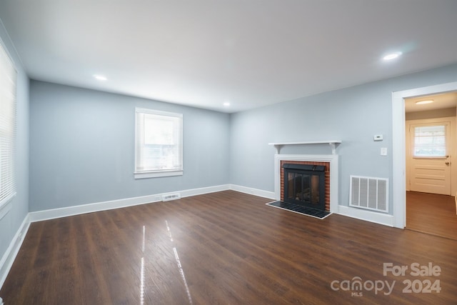 unfurnished living room featuring dark hardwood / wood-style floors, a brick fireplace, and a wealth of natural light