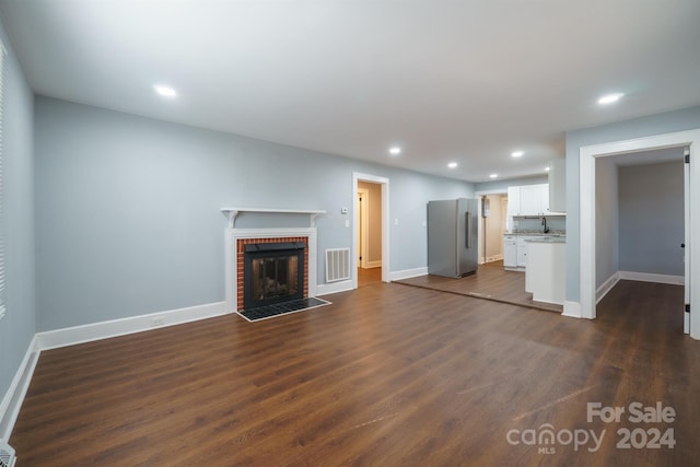 unfurnished living room featuring dark hardwood / wood-style flooring and a brick fireplace