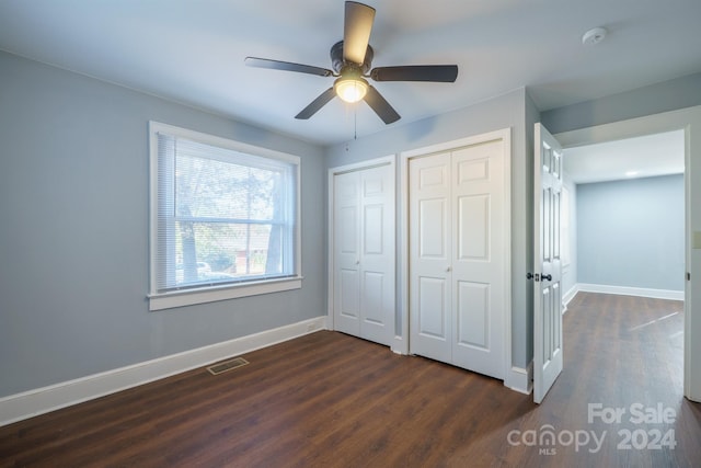 unfurnished bedroom with two closets, ceiling fan, and dark hardwood / wood-style floors