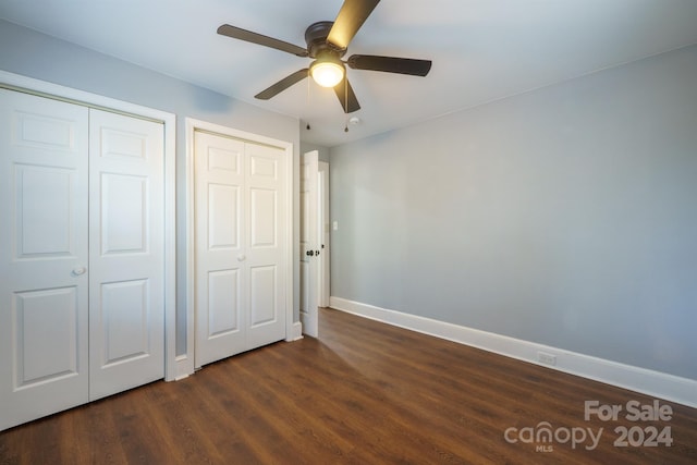 unfurnished bedroom featuring ceiling fan, dark wood-type flooring, and two closets