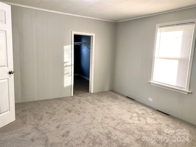 unfurnished bedroom featuring a walk in closet, wood walls, a closet, and carpet floors