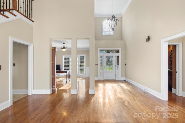 entryway featuring crown molding, a towering ceiling, a chandelier, and hardwood / wood-style flooring