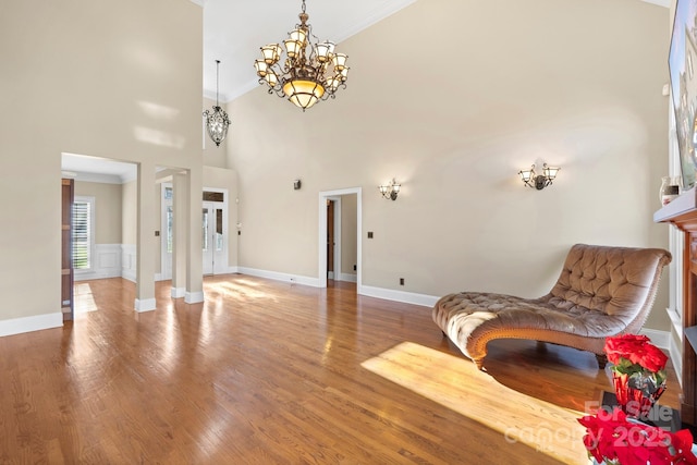 living area featuring a chandelier, a high ceiling, ornamental molding, and hardwood / wood-style floors