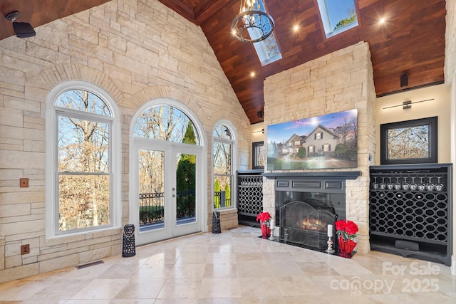 living room featuring french doors, a skylight, an outdoor stone fireplace, high vaulted ceiling, and wooden ceiling