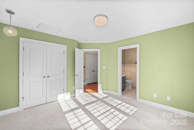 unfurnished bedroom featuring light colored carpet, ensuite bath, and a closet