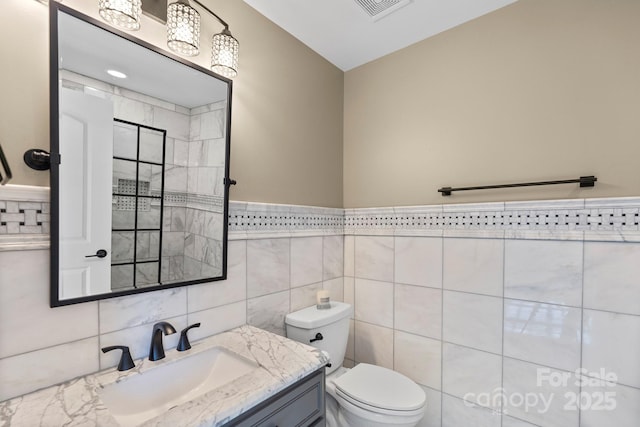 bathroom with vanity, tile walls, and toilet