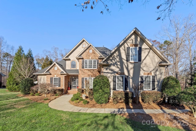 traditional-style home featuring brick siding, a front yard, and roof with shingles