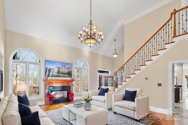 living room featuring wood finished floors, a glass covered fireplace, baseboards, a towering ceiling, and stairs