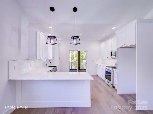 kitchen with white cabinetry, sink, kitchen peninsula, decorative light fixtures, and appliances with stainless steel finishes