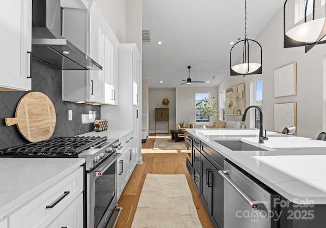 kitchen with stainless steel appliances, white cabinetry, wall chimney range hood, and decorative light fixtures