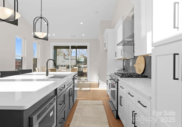 kitchen with hanging light fixtures, white cabinetry, a center island with sink, and high end range