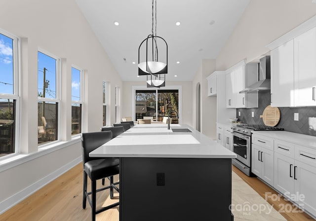 kitchen featuring high end stainless steel range, an island with sink, wall chimney range hood, decorative backsplash, and white cabinets