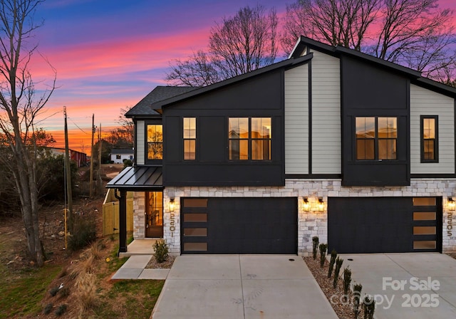 modern home featuring a garage, stone siding, concrete driveway, and a standing seam roof