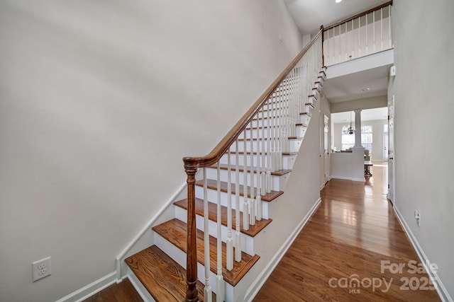 stairs with a chandelier, hardwood / wood-style floors, and a towering ceiling