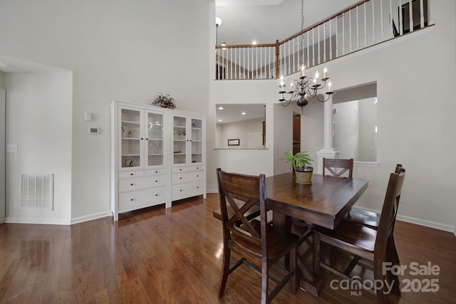 dining area featuring a towering ceiling, decorative columns, dark wood-type flooring, and a notable chandelier