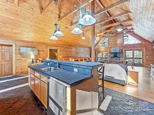 kitchen with a kitchen island with sink, sink, high vaulted ceiling, and wood walls