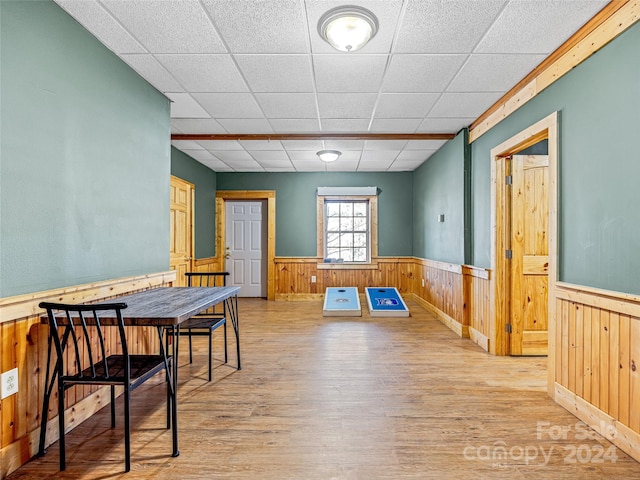 dining area with wood walls, a drop ceiling, and light hardwood / wood-style floors