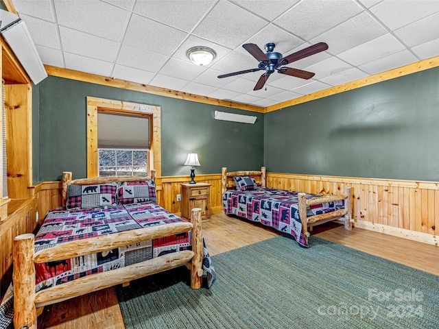 bedroom with a paneled ceiling, ceiling fan, wood walls, and hardwood / wood-style flooring