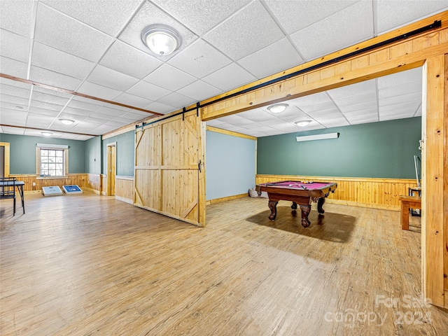 recreation room featuring a barn door, wood walls, a drop ceiling, and wood-type flooring