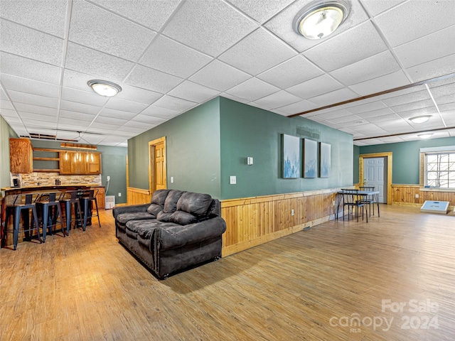 living room featuring a paneled ceiling, light hardwood / wood-style flooring, and wood walls