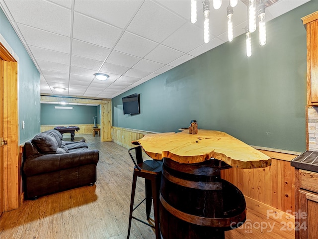 dining space featuring light wood-type flooring, a drop ceiling, and wooden walls