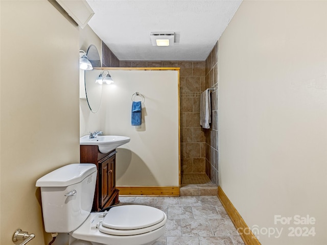 bathroom with a tile shower, vanity, a textured ceiling, and toilet