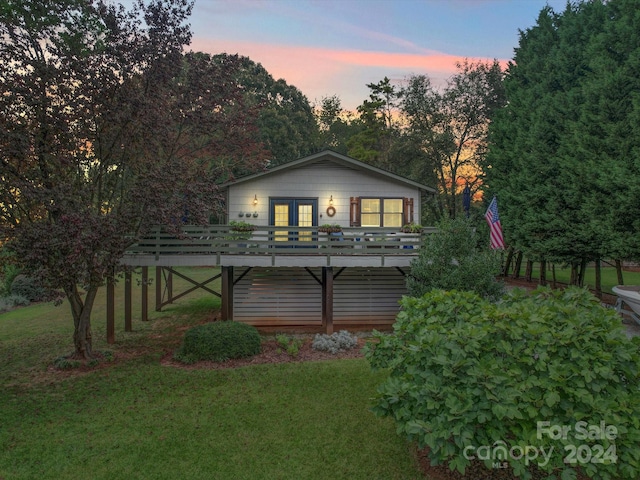 back house at dusk with a yard, french doors, and a deck