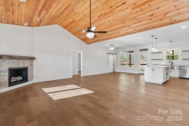 unfurnished living room with light wood-type flooring, ceiling fan, sink, a barn door, and wooden ceiling