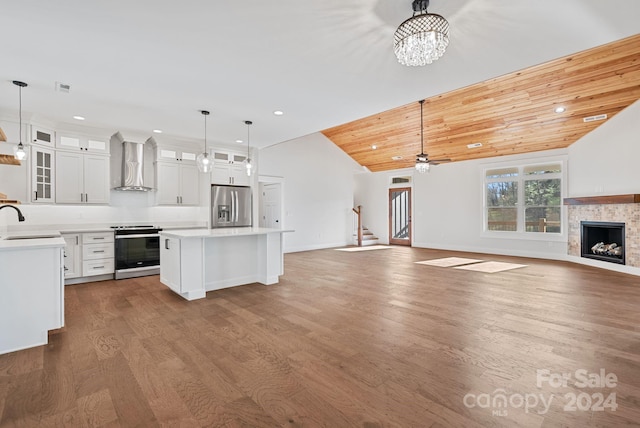 kitchen with appliances with stainless steel finishes, wall chimney range hood, pendant lighting, white cabinets, and hardwood / wood-style floors