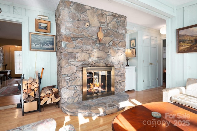 living room featuring wood walls, ornamental molding, light hardwood / wood-style flooring, and a stone fireplace