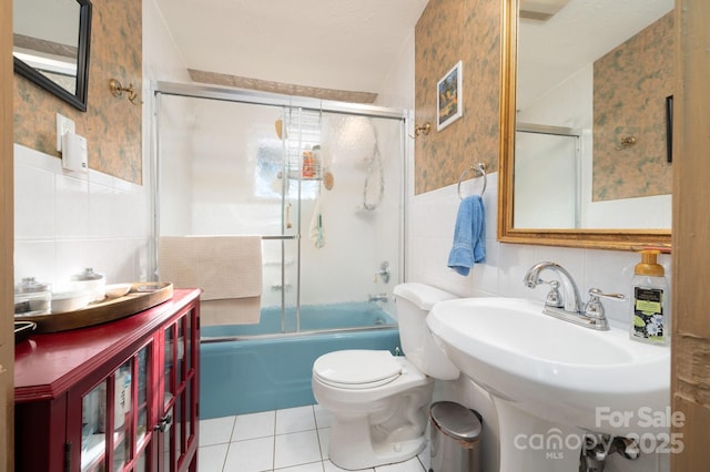 full bathroom with toilet, a textured ceiling, tile walls, bath / shower combo with glass door, and tile patterned floors