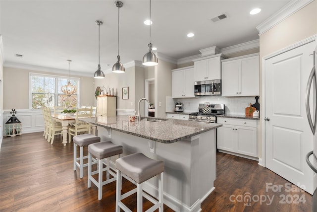 kitchen with white cabinets, dark hardwood / wood-style floors, an island with sink, decorative light fixtures, and stainless steel appliances