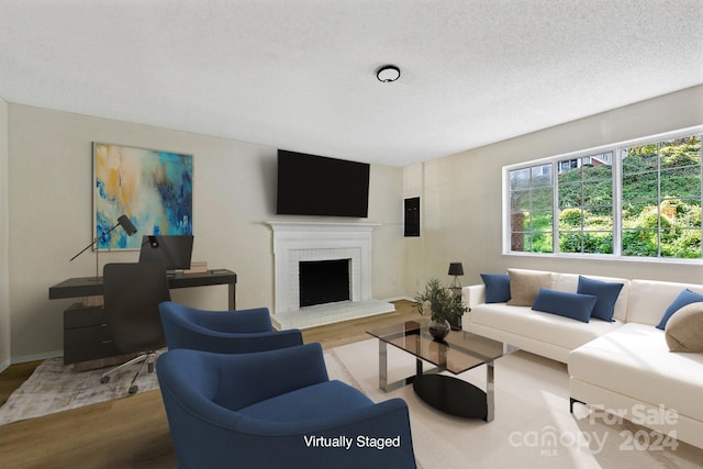 living room with wood-type flooring, a textured ceiling, and a brick fireplace