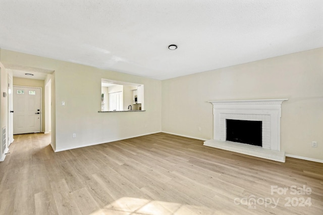 unfurnished living room featuring a textured ceiling, light wood-type flooring, and a brick fireplace