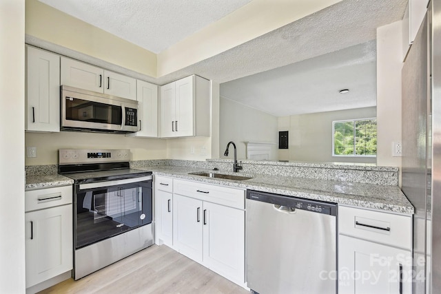 kitchen featuring white cabinets, sink, a textured ceiling, light hardwood / wood-style floors, and stainless steel appliances