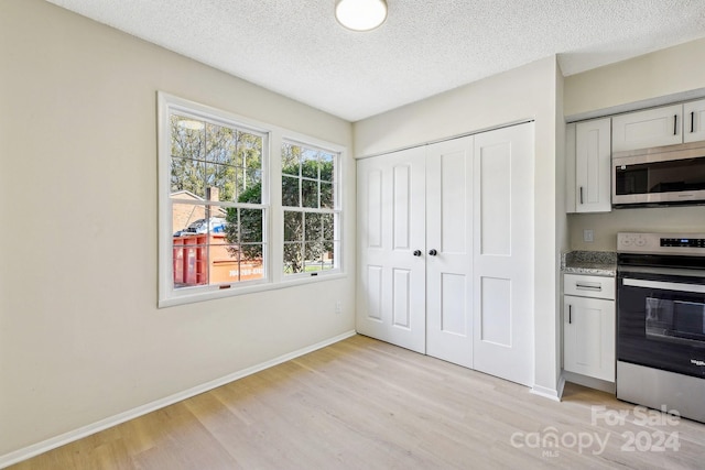 kitchen with white cabinets, light wood-type flooring, stainless steel appliances, and a textured ceiling