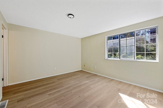 empty room with light wood-type flooring and a textured ceiling