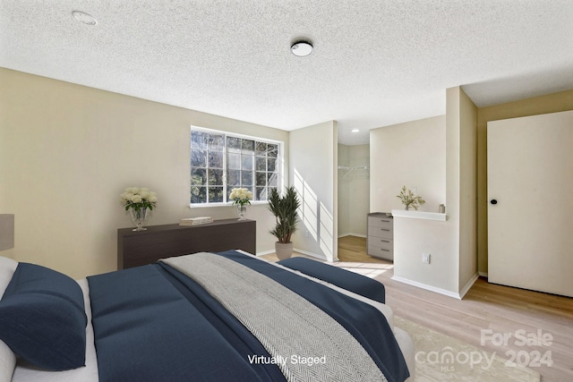 bedroom featuring a spacious closet, a closet, light hardwood / wood-style floors, and a textured ceiling