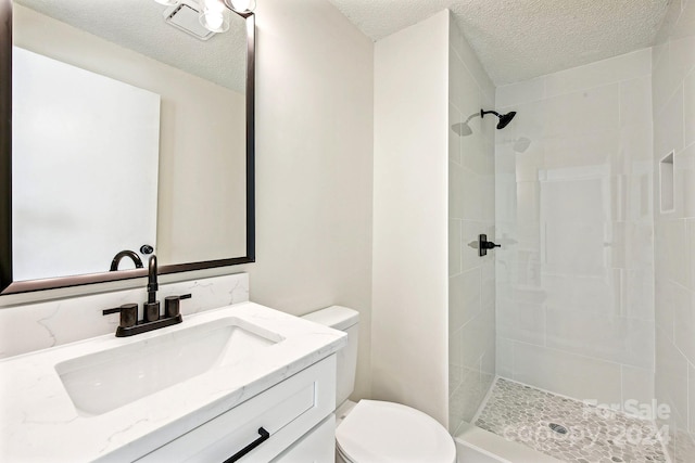 bathroom with a tile shower, vanity, a textured ceiling, and toilet