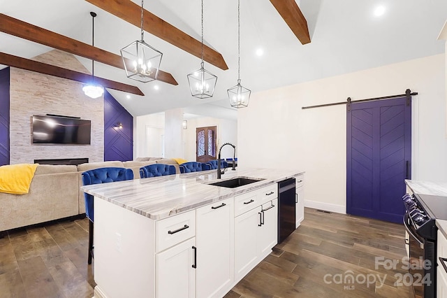 kitchen with white cabinets, hanging light fixtures, a barn door, light stone countertops, and an island with sink