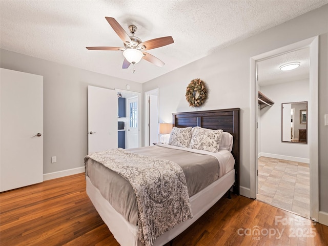 bedroom featuring a walk in closet, a textured ceiling, ceiling fan, hardwood / wood-style flooring, and a closet