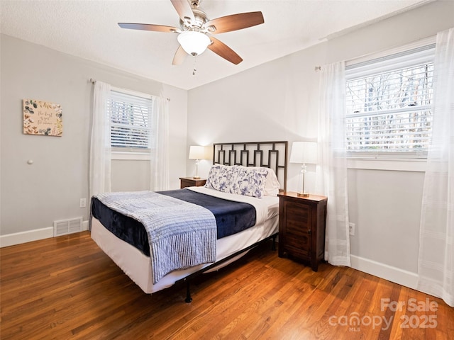 bedroom with multiple windows, ceiling fan, dark wood-type flooring, and a textured ceiling